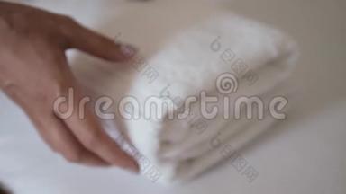 双手特写，把一叠新鲜的白色浴巾放在床单上。 客房服务员清洁酒店客房